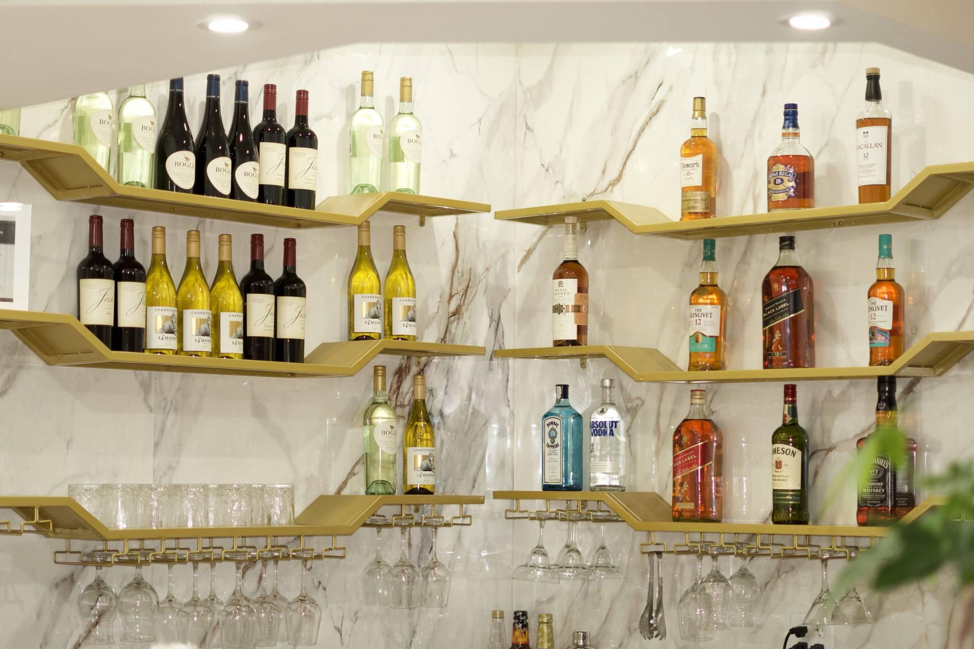 Our bar: wine and whiskey on gold shelves against white marble, with glasses hanging below